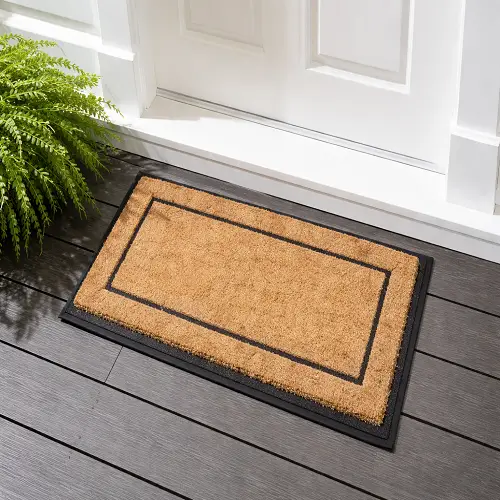 Natural brown coir mat with a black border placed at a home doorway, designed to trap dirt and moisture while providing a durable and decorative welcome at the entrance
